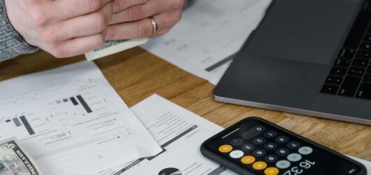 Hands counting money at a workspace with a laptop, calculator, and financial documents.