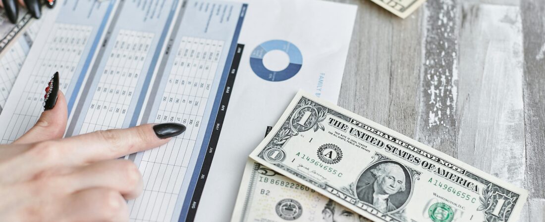 Close-up of hands analyzing financial document with US dollar bills on table.